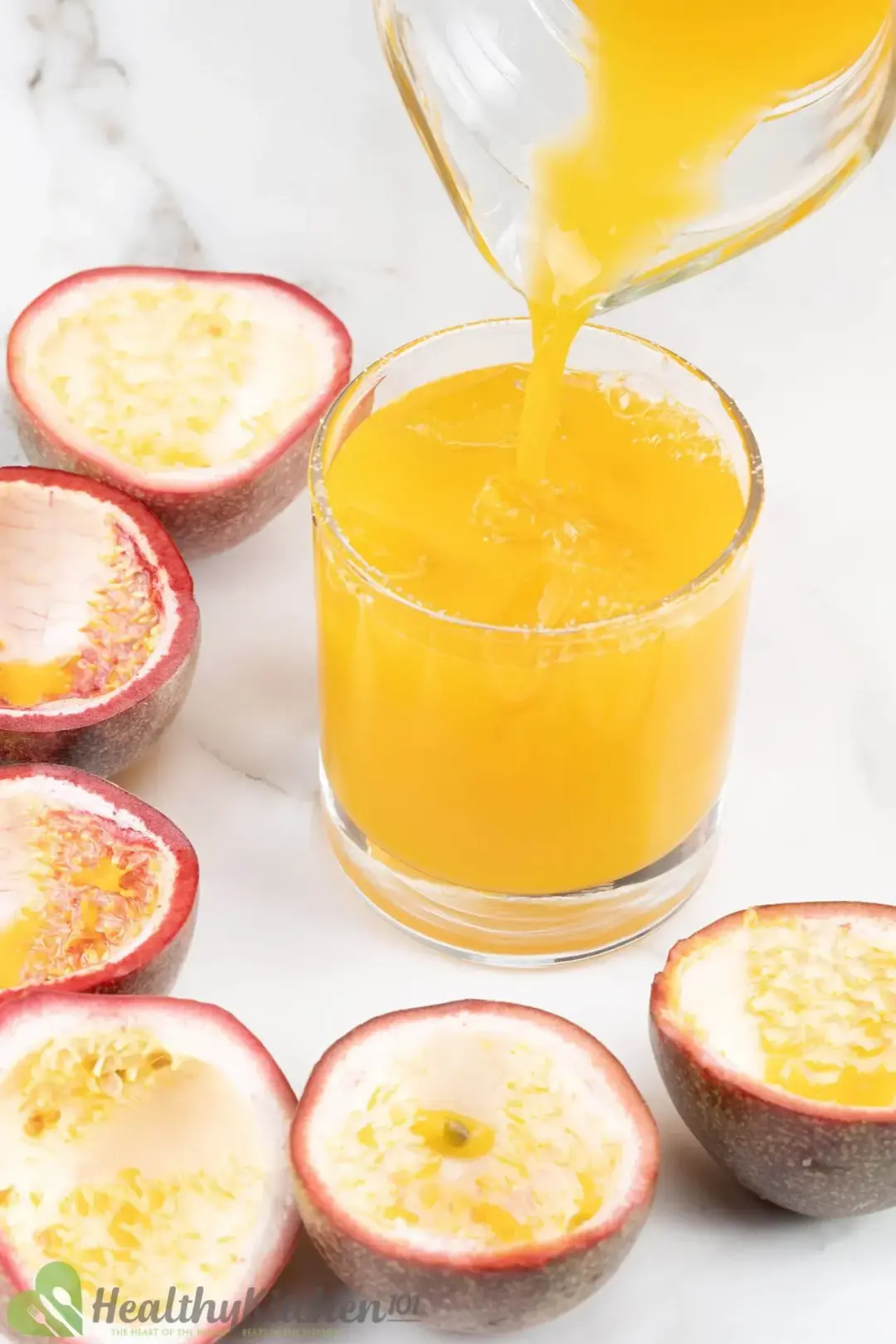 Pouring a passion fruit margarita into a short glass with ice, next to hollow shells of passion fruits