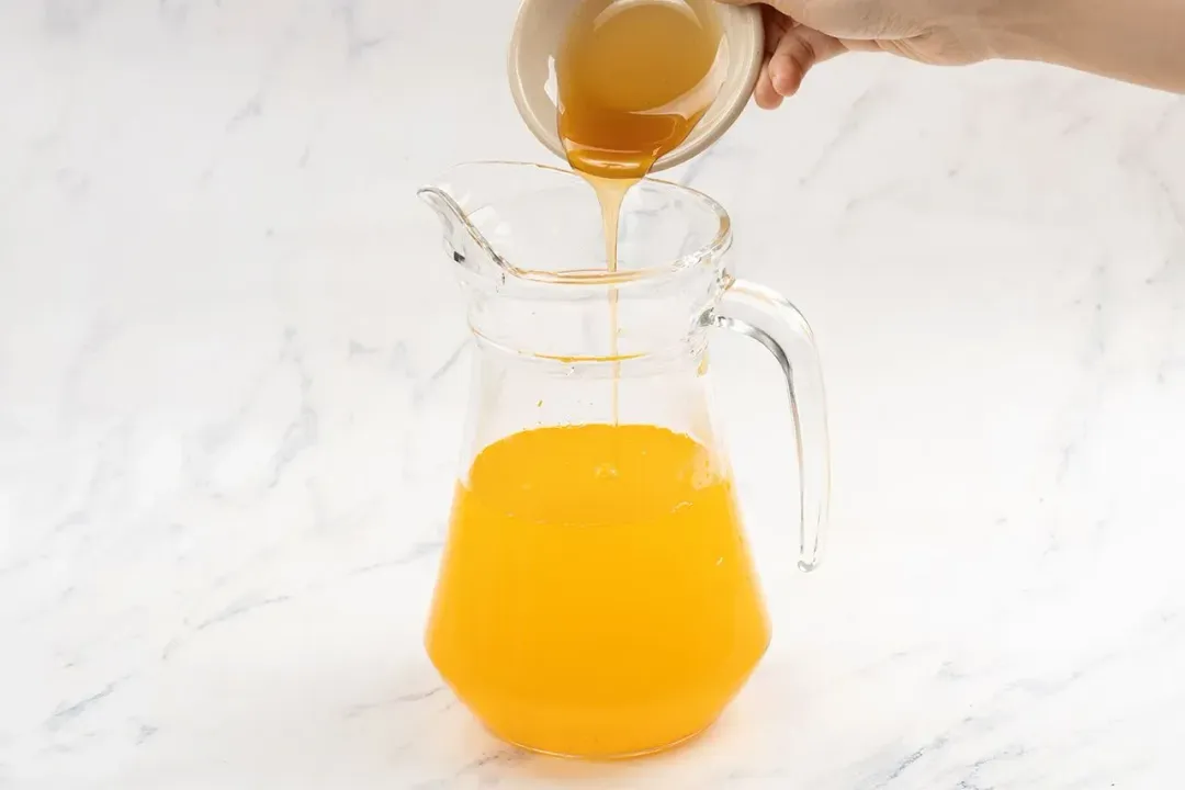 hand holding a bowl of honey pouring into a pitcher of turmeric and apple cider vinegar