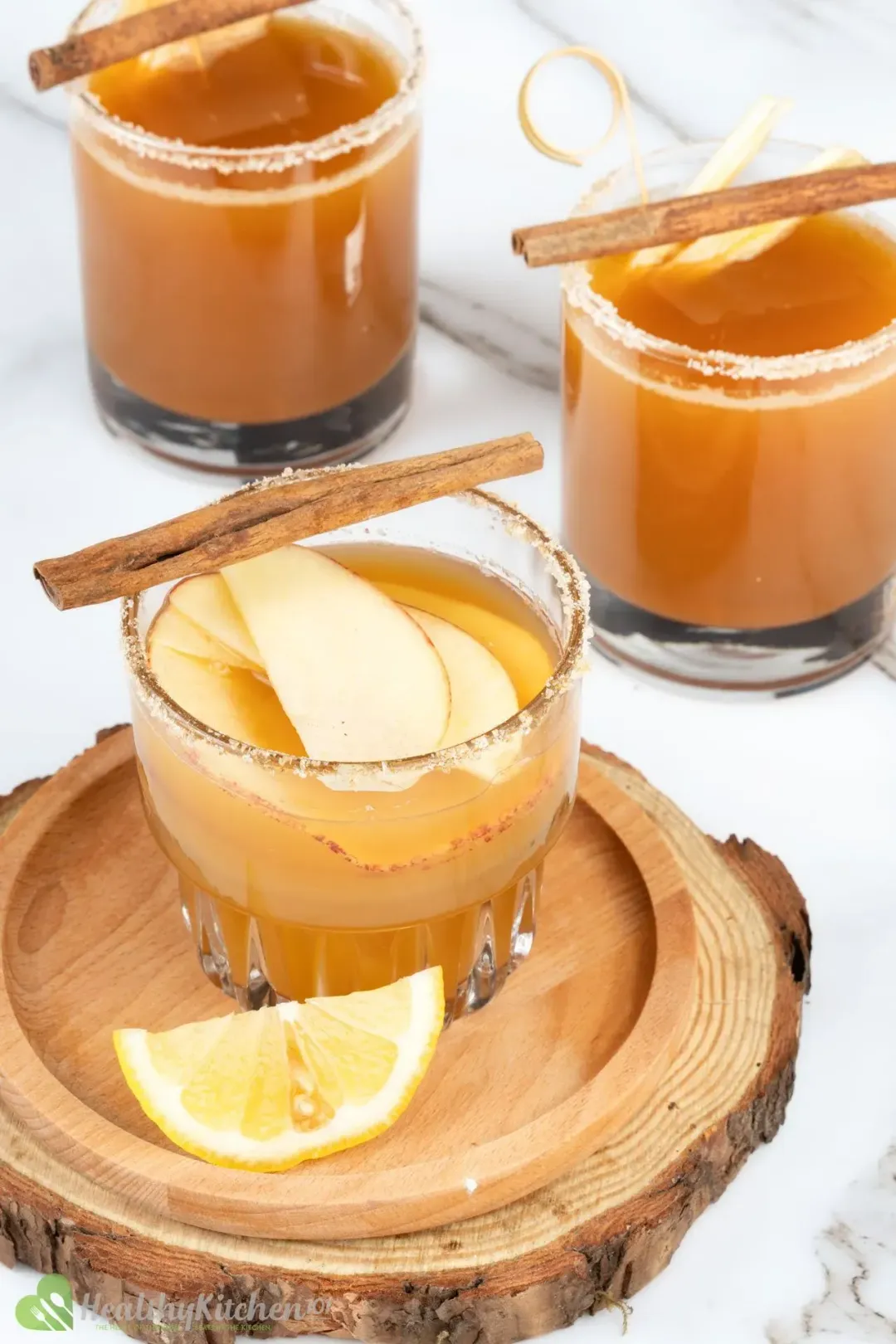 Three glasses of apple juice and vodka cocktail, topped with cinnamon sticks and sliced apples, put on a wooden tray