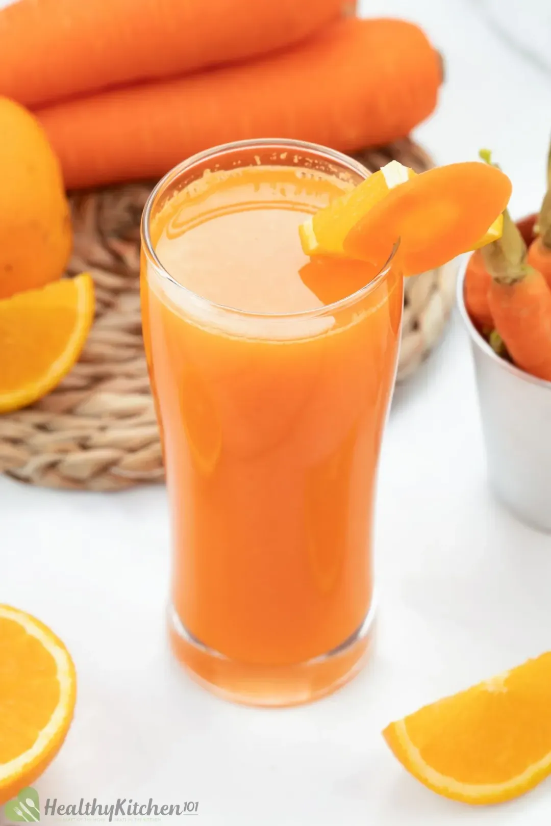 A tall glass of carrot orange juice next to some orange wedges, carrots