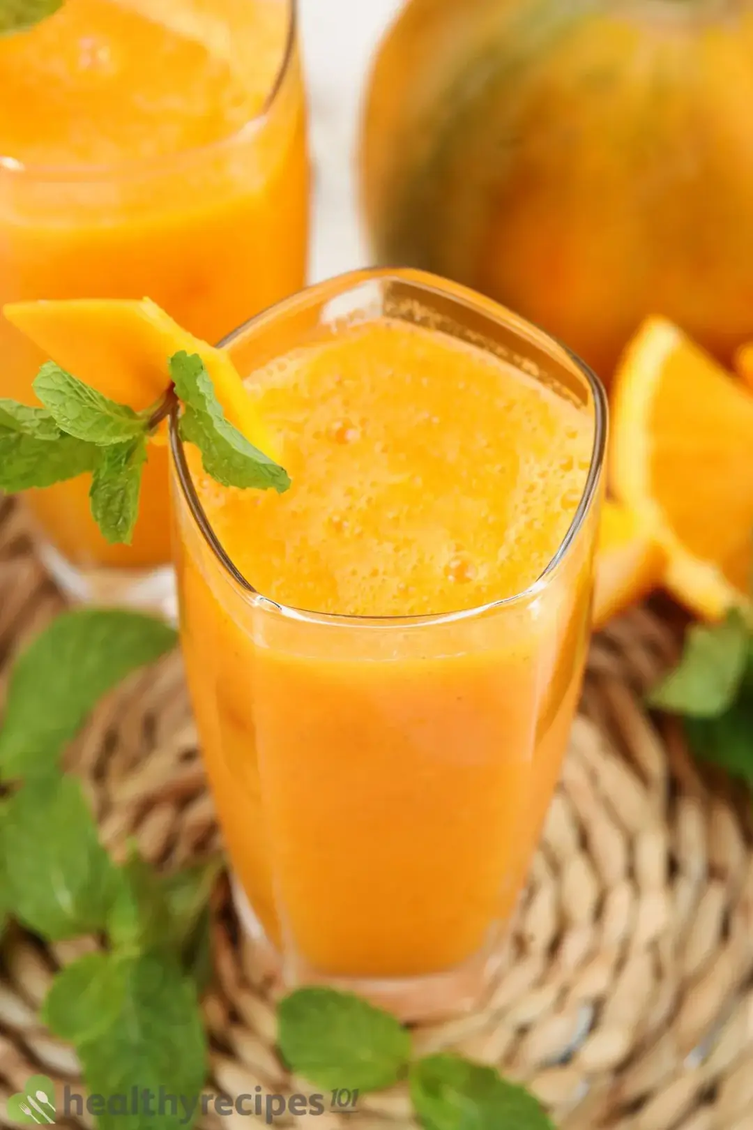 Two glasses of papaya juice, next to some mint leaves and orange wedges