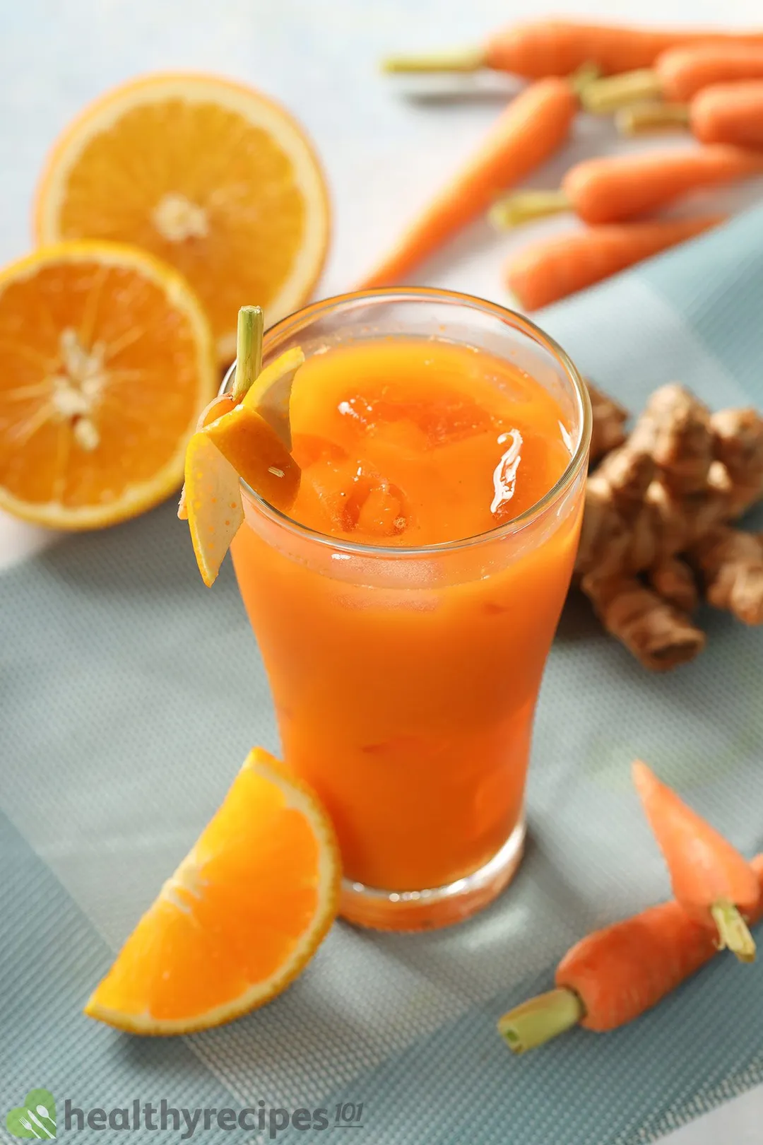 a glass of carrot turmeric juice, decorated with carrot, half orange, turmeric root