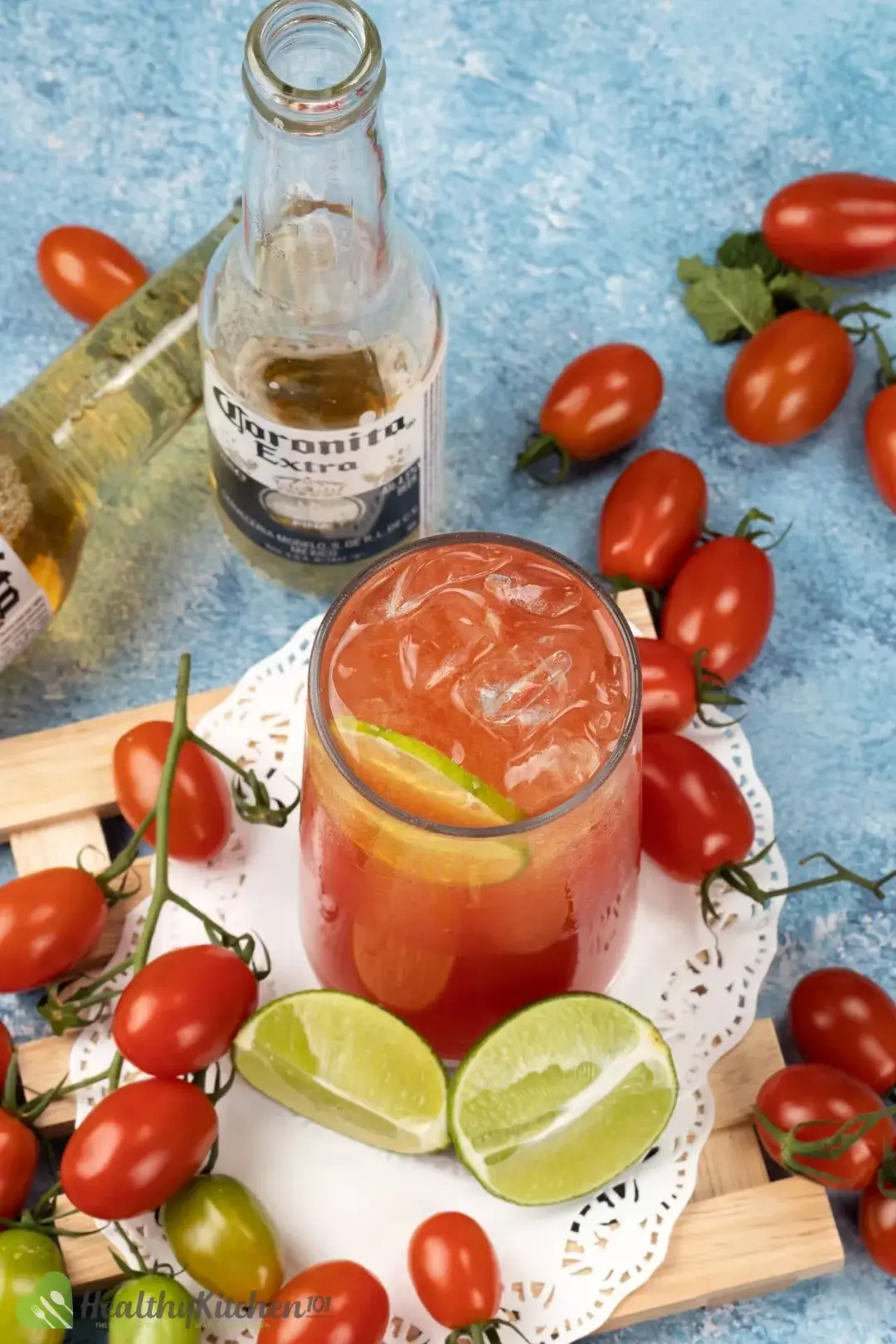 A shot from the top of an iced beer and tomato cocktail surrounded by cherry tomatoes, lime wedges, and beer bottles