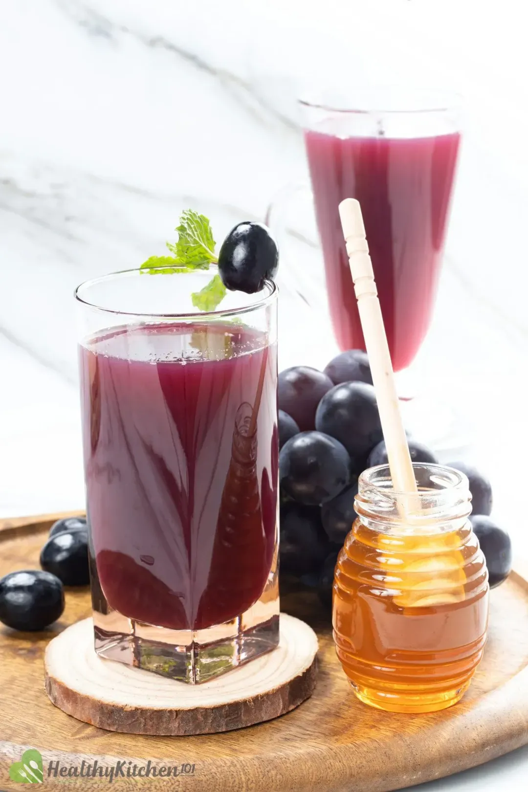 A tall glass of apple cider vinegar and grape juice next to a grape vine and a honey jar