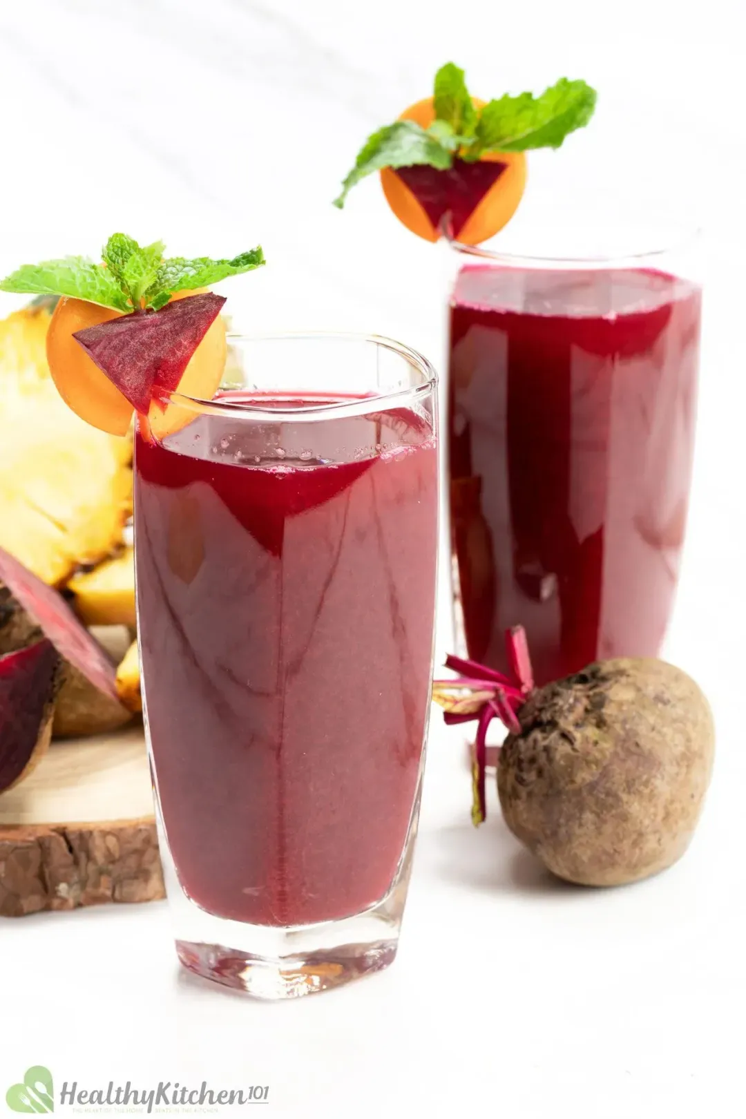 Two glasses of beet juice next to a beetroot and some pineapples in the back