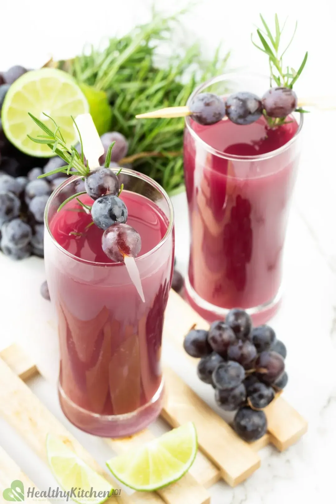 A shot from the top of two grape juice glasses next to some grapes, rosemary, and limes