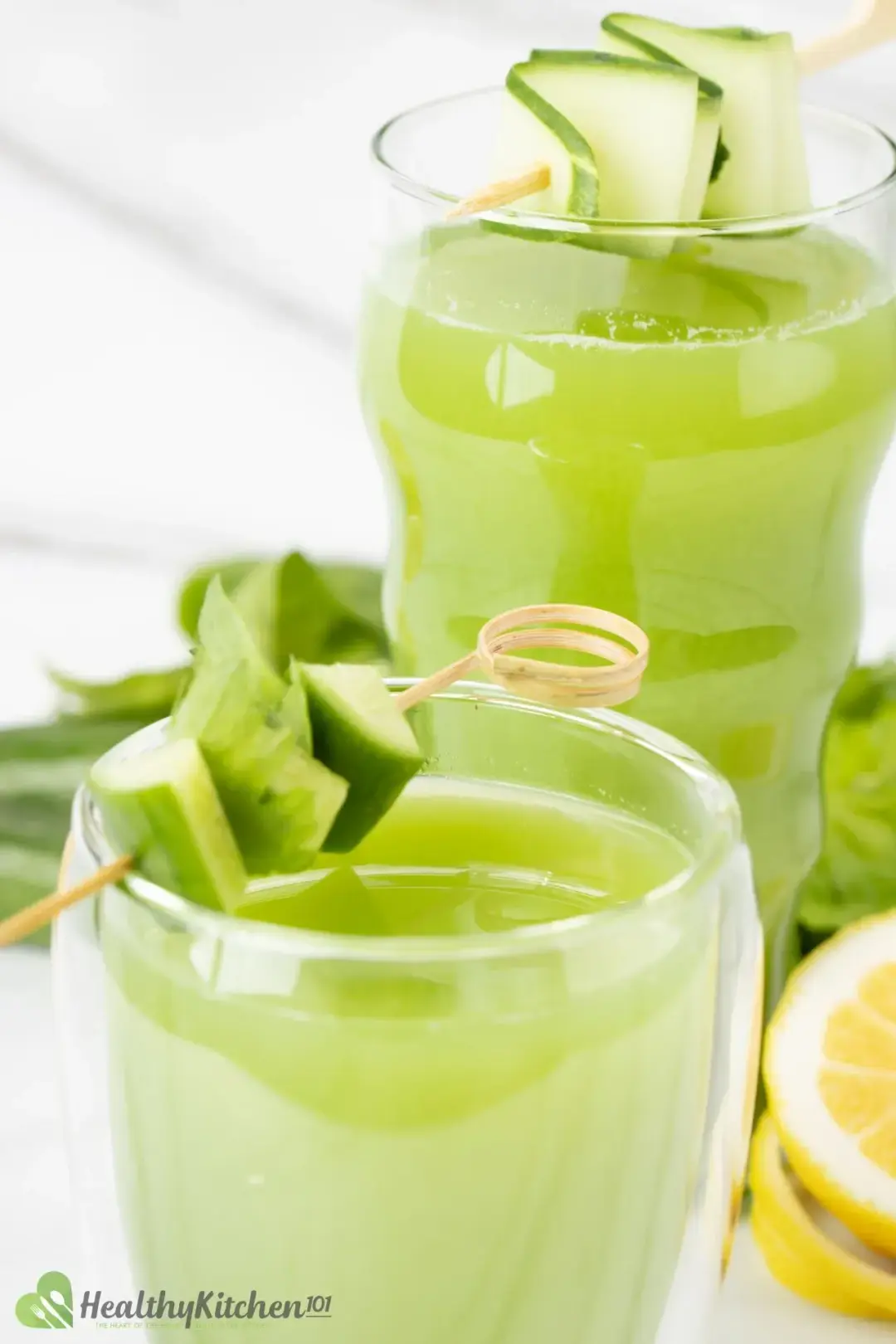 Two glasses of cucumber celery drink, each with a skewered strand of cucumber slice on top