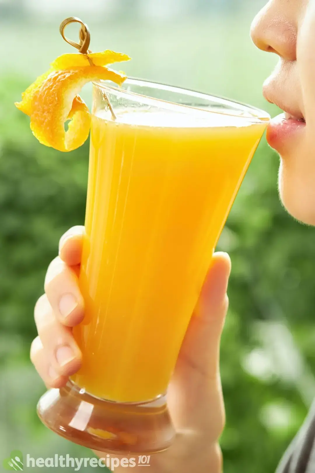 A person drinking a glass of orange juice filled all the way to the top