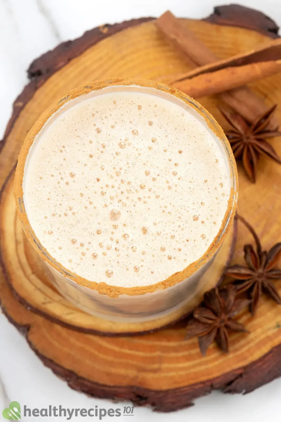 A foamy frothy eggnog inside a glass with star anise around on a wooden coaster