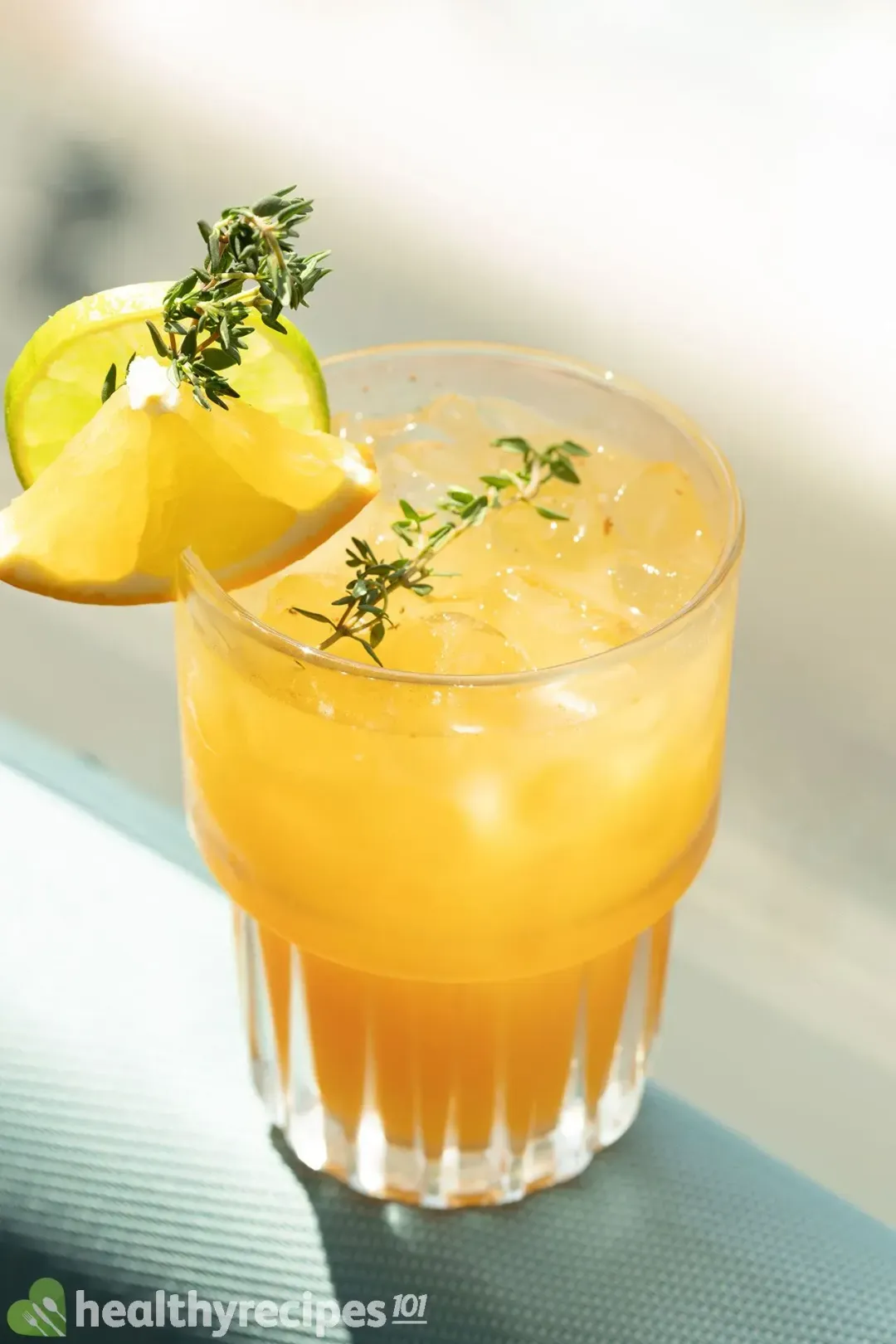 An iced glass of grapefruit cocktail with thyme sprigs and citrus wheels on the rim