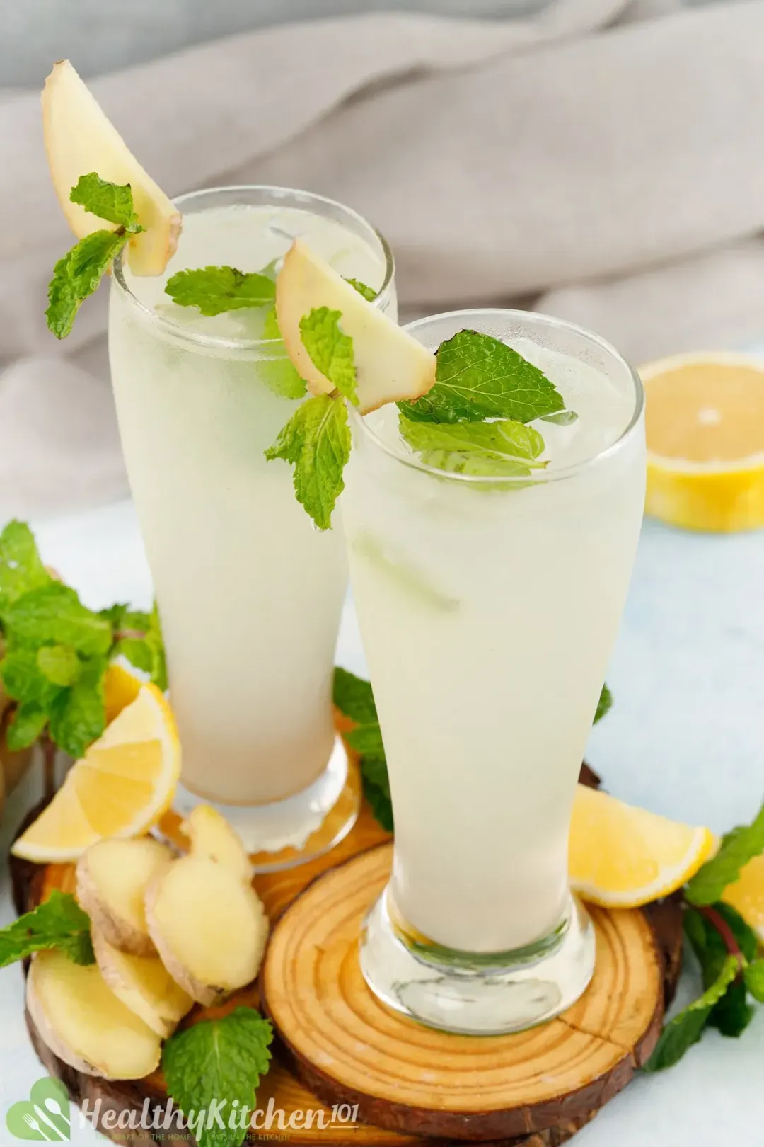 Two tall glasses of white ginger lemonade garnished with loads of mints, lemon wedges, and ginger slices