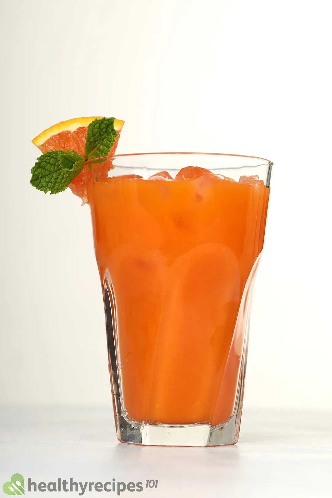 a glass of grapefruit carrot juice decorated with mint and grapefruit slice