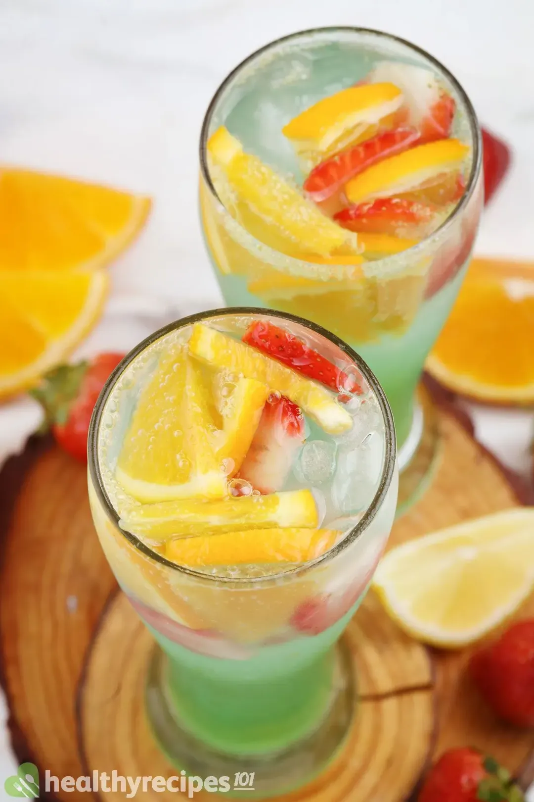 A high-angle shot of green juice glasses containing lemon slices, strawberry slices, and some ice