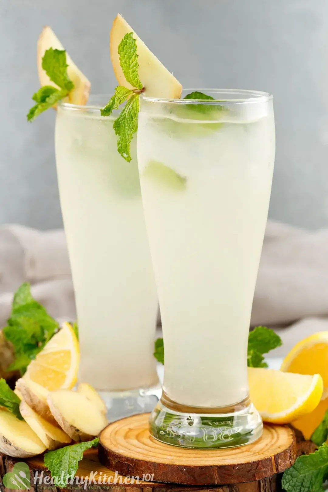 Two tall glasses of iced white lemonade garnished with mint leaves, lemon wedges, and ginger slices