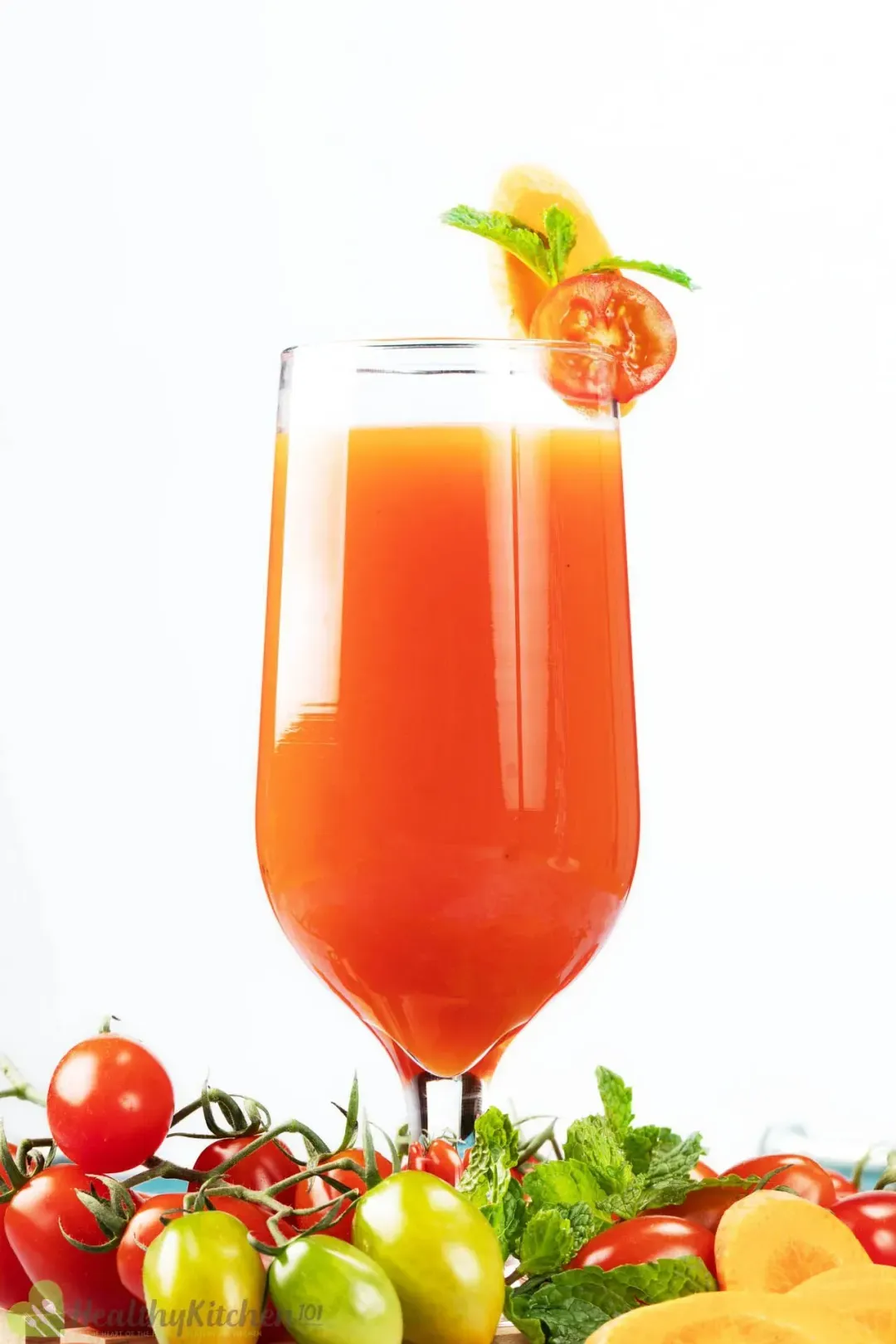 A glass of orange and tomato juice surrounded by cherry tomatoes of different colors