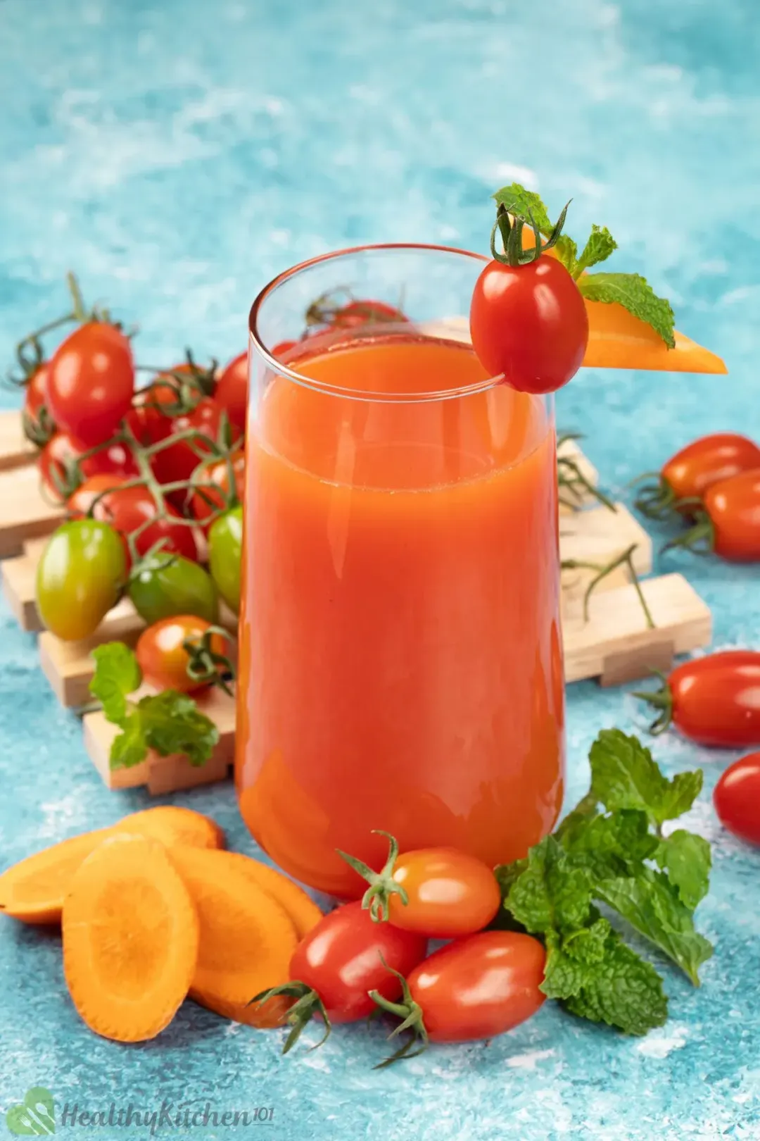 A glass of cherry tomato carrot juice surrounded by cherry tomatoes and garnishes