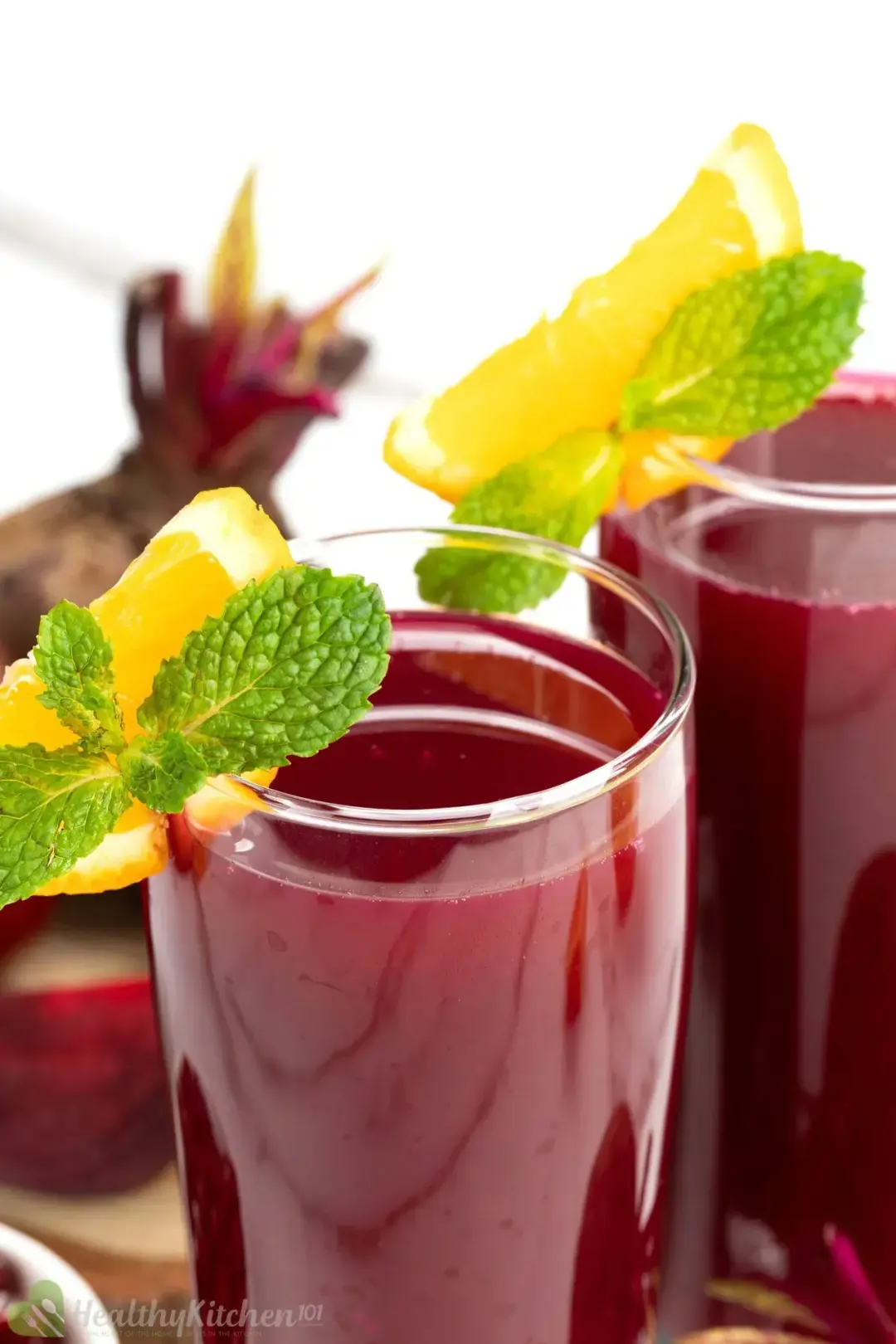 Two glasses of beetroot juice decorated with orange wedges, mints, and whole beetroots