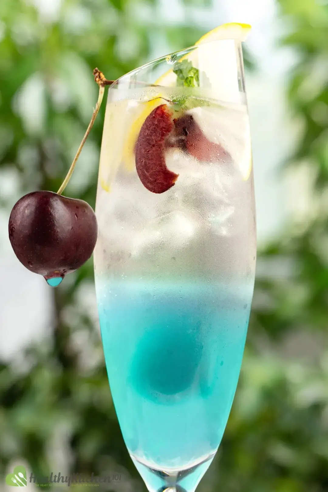 A cocktail glass of a cyan-hued drink, topped with ice, cherries, and mints
