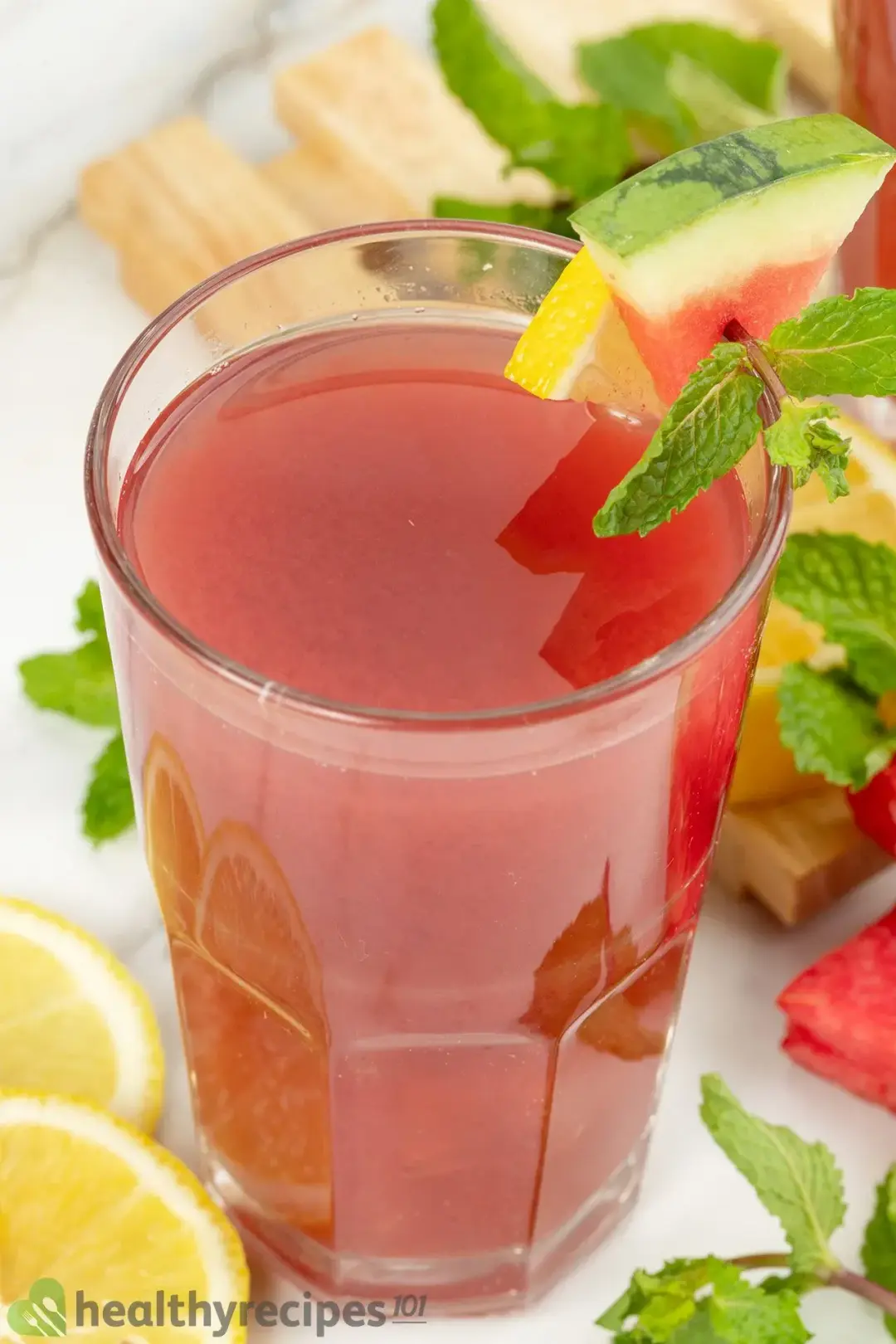 A high-angle shot of a glass of watermelon cucumber juice decorated by a piece of lemon, a piece of watermelon, and mint leaves