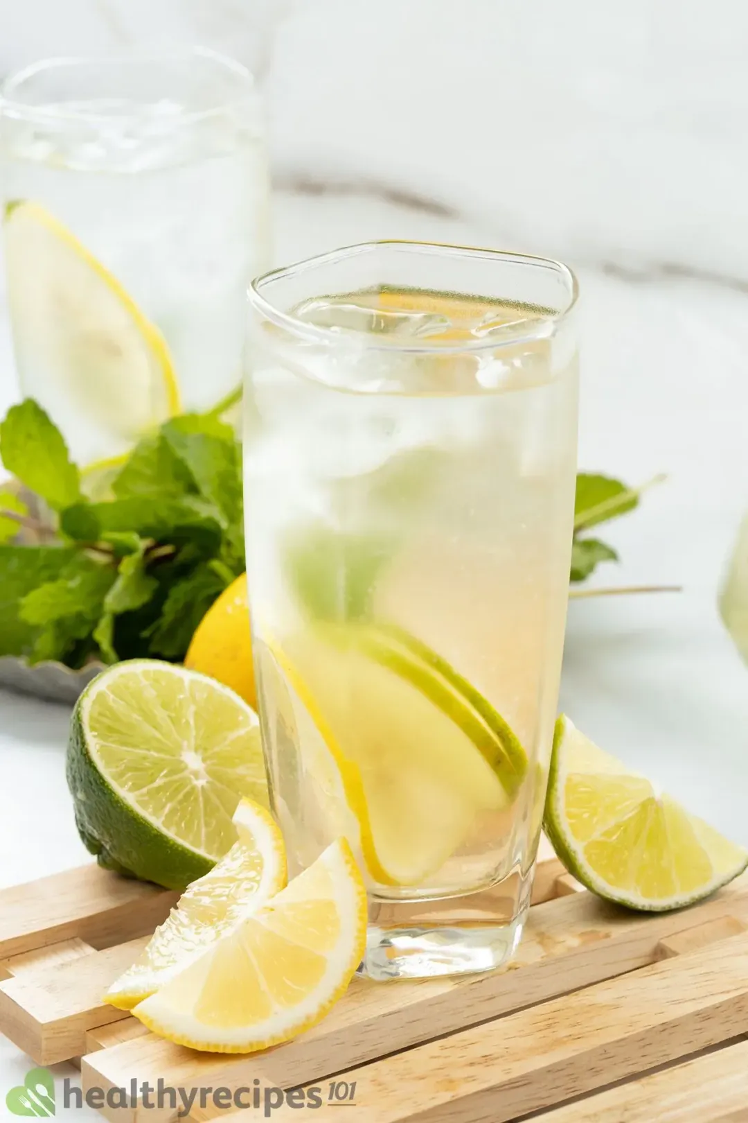 A glass of citrus wheels, ice, and water on a wooden board with citrus wedges and mints