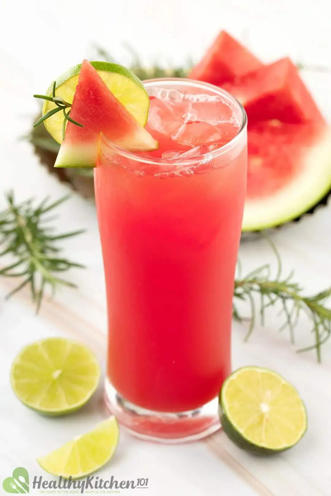 An iced glass of watermelon drink, garnished with lime wheels and watermelon in the background