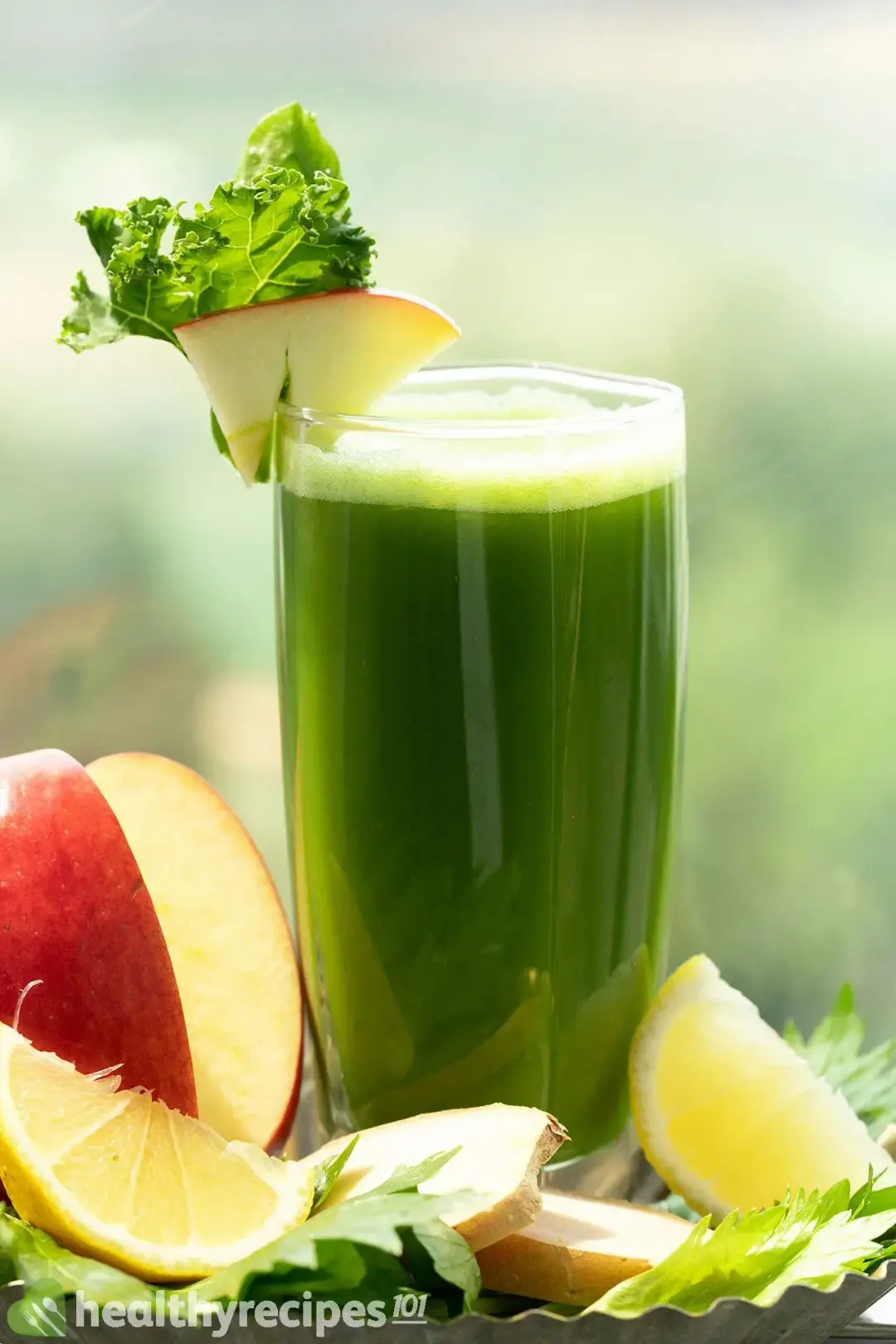 A glass of mean green juice put next to an apple and lemon wedges, taken outdoor