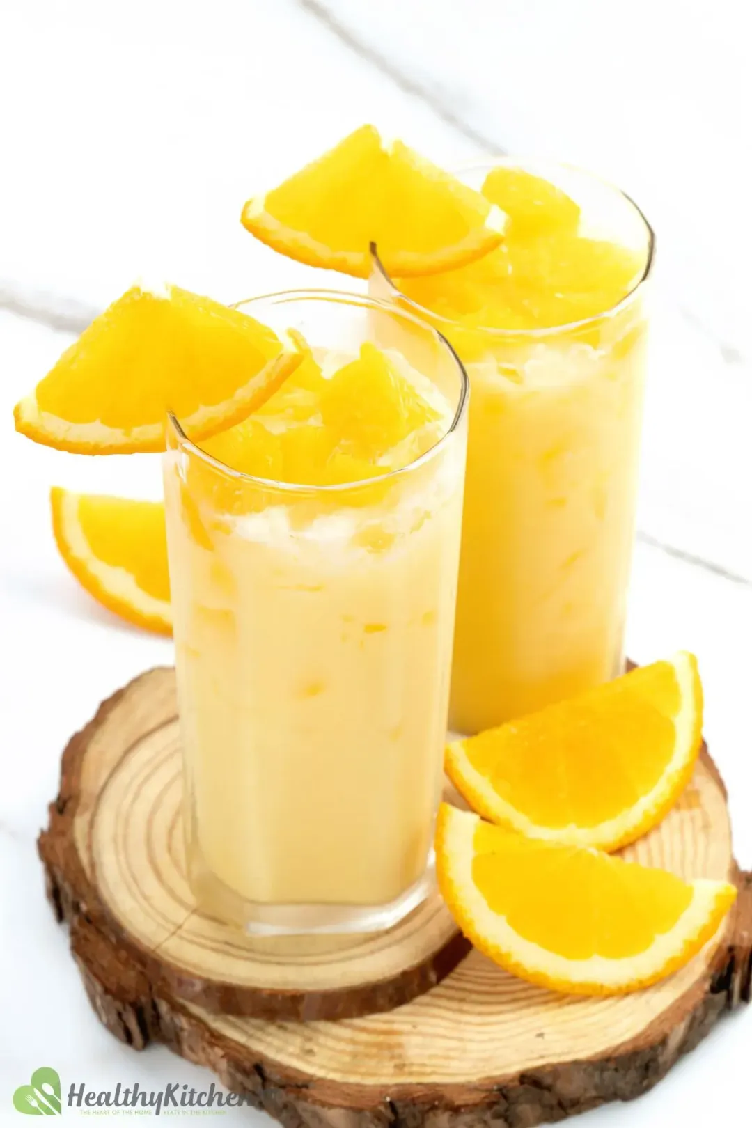 Two tall glasses of milk and orange drink, full of cubed oranges and orange wedges as garnish