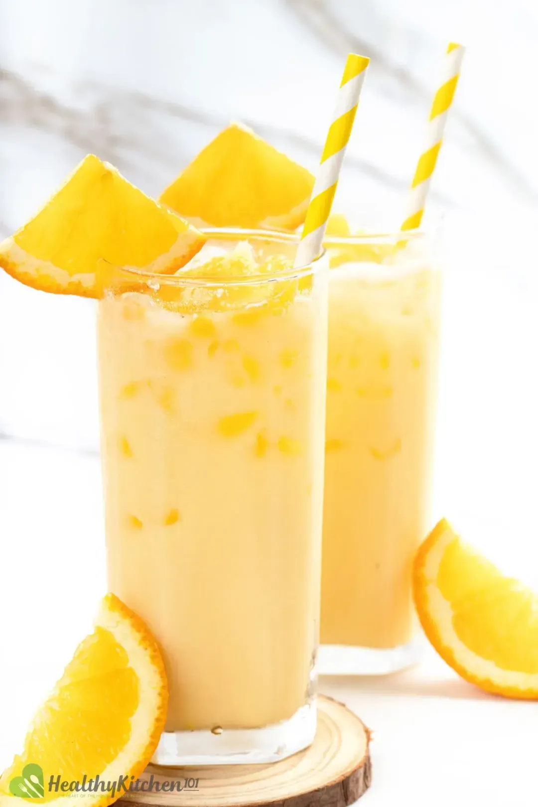 Two tall glasses full of orange juice and milk drink, full of ice, and garnished with orange wedges