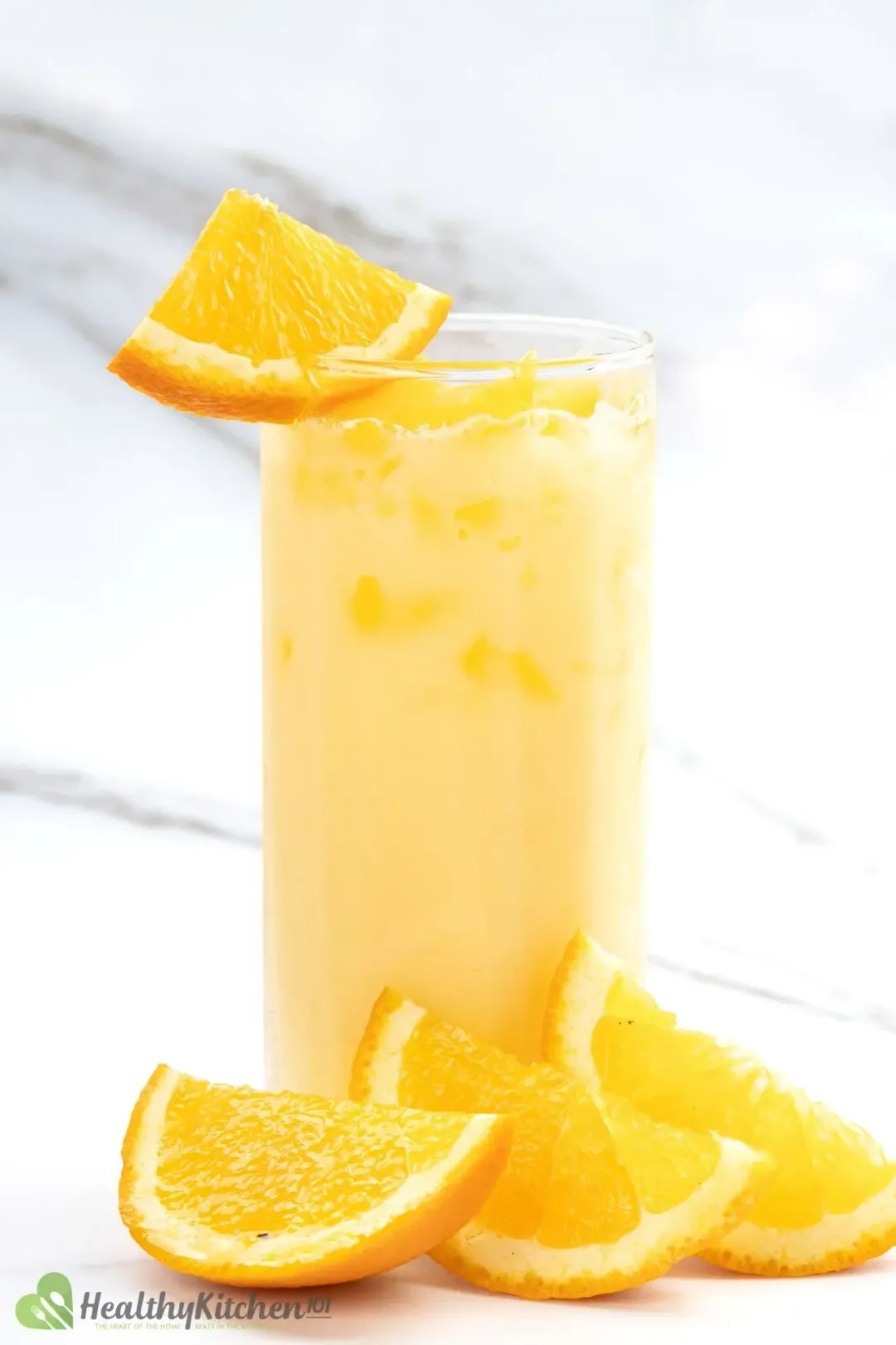 A tall glass of a milk and orange drink, garnished with orange wedges