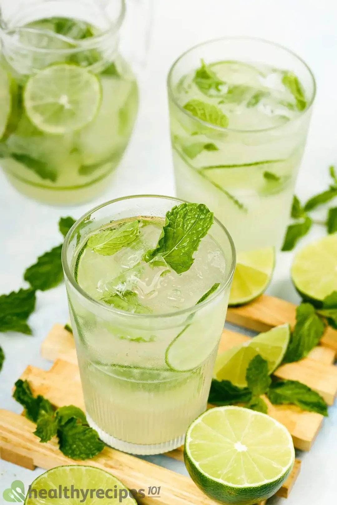 Three glasses of iced mojitos, with lime wedges and mint leaves lying around