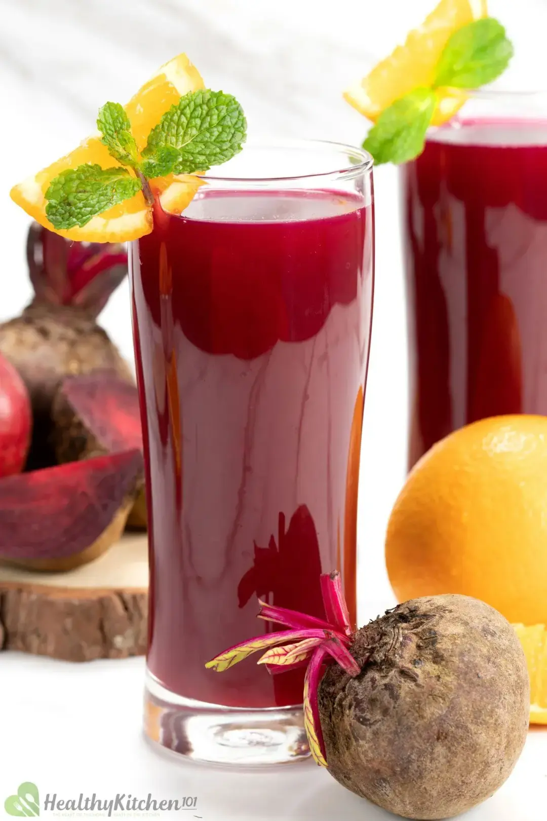 Two glasses of beetroot juice decorated with orange wedges, mints, and whole beetroots