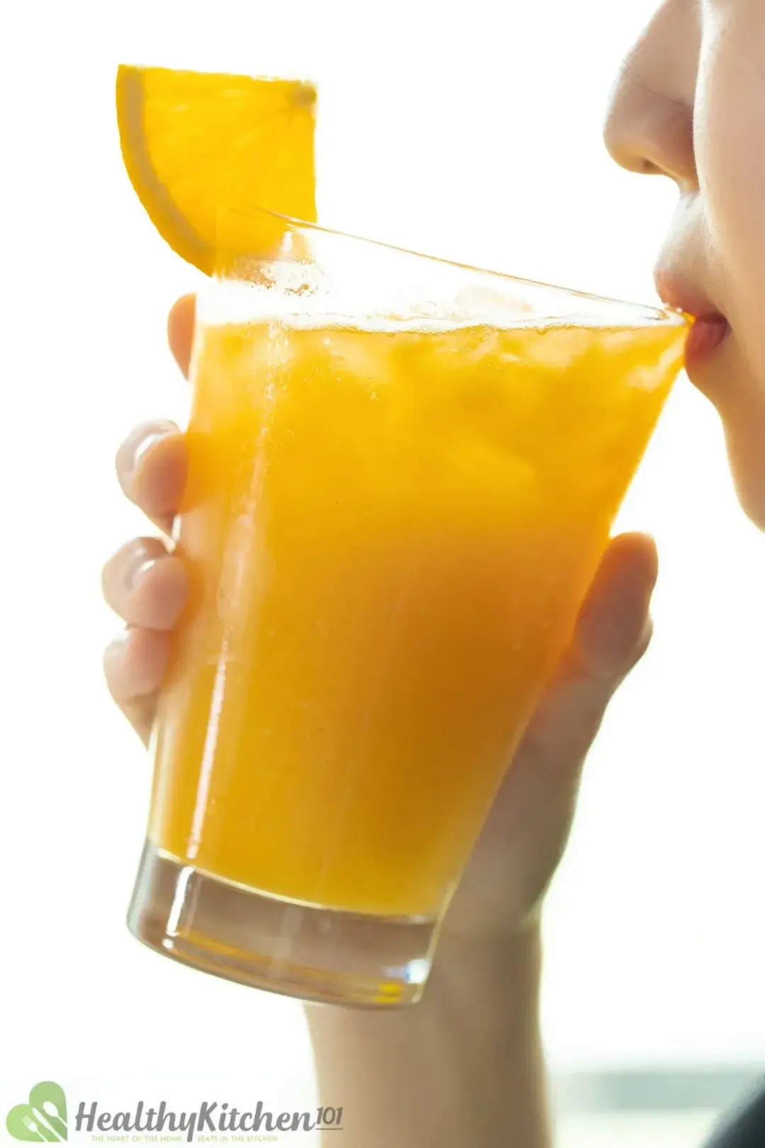 A person sipping a glass of ice orange juice