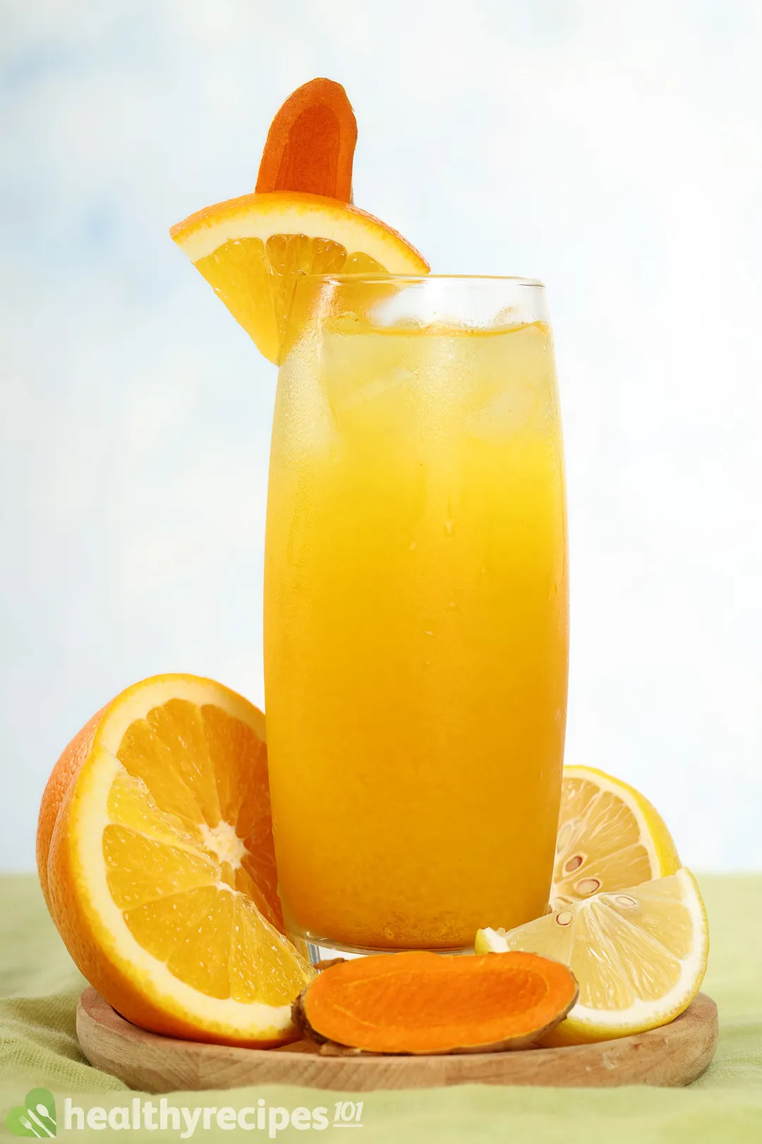 a glass of orange turmeric juice decorated with orange slices turmeric slices