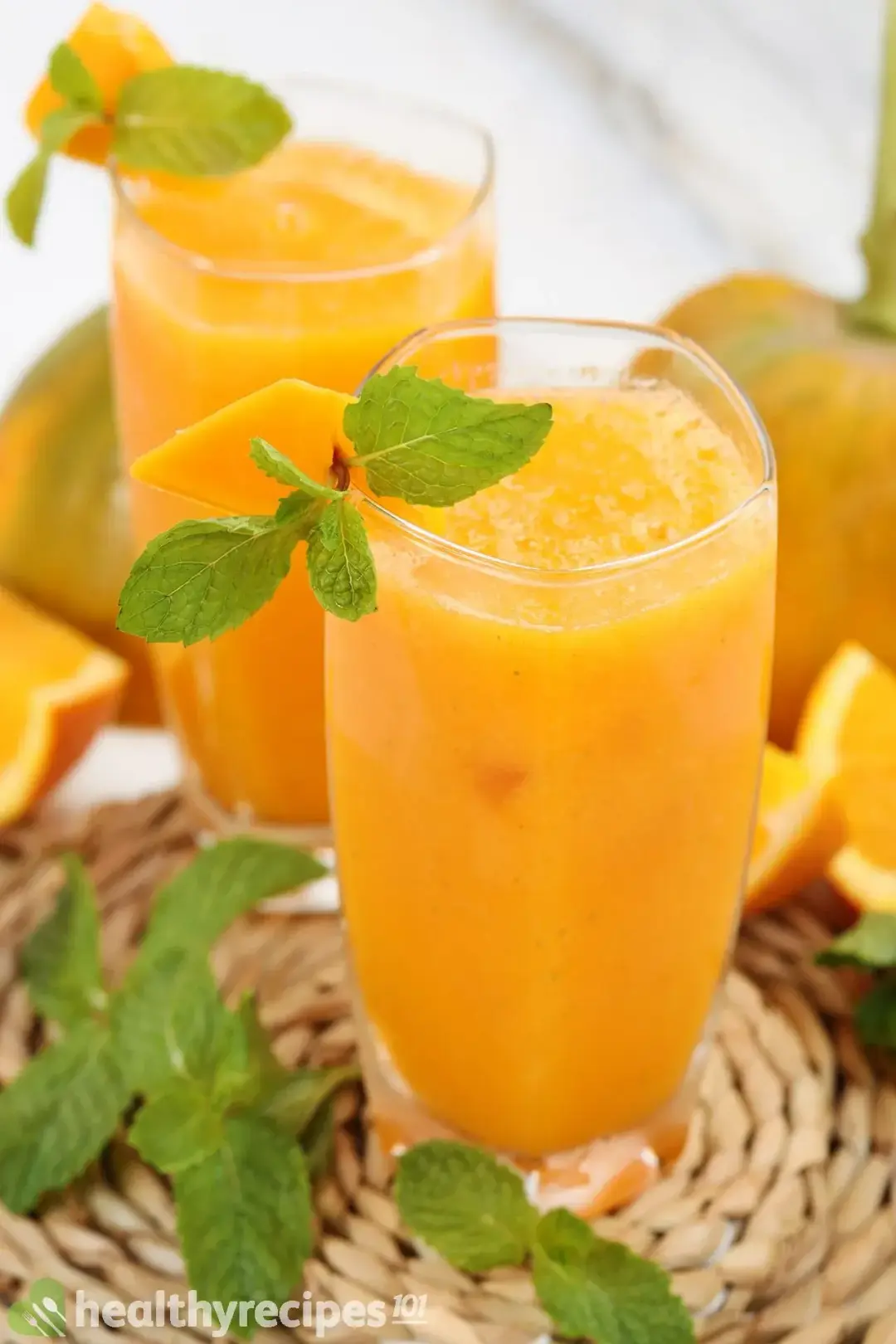 Two glasses of Papaya Juice side by side decorated with mint leaf, orange sliced and papaya