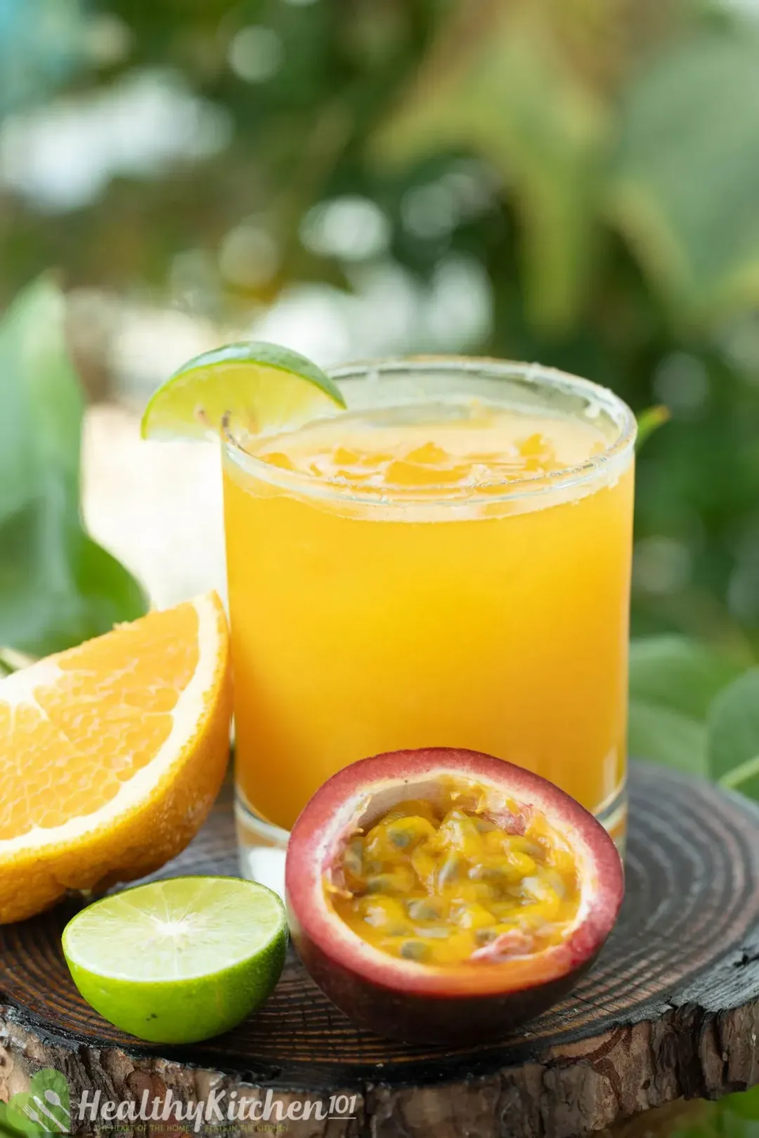A short glass of passion fruit margarita next to an orange wedge, lime half, and halved passion fruit