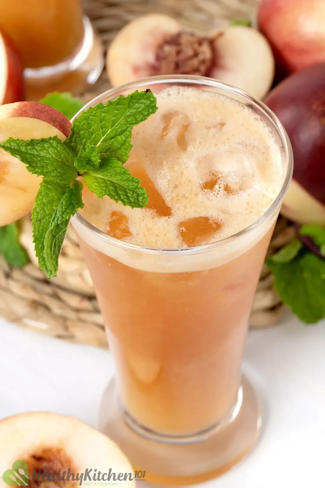 A short glass of peach juice with ice, next to peach halves and lots of mint leaves