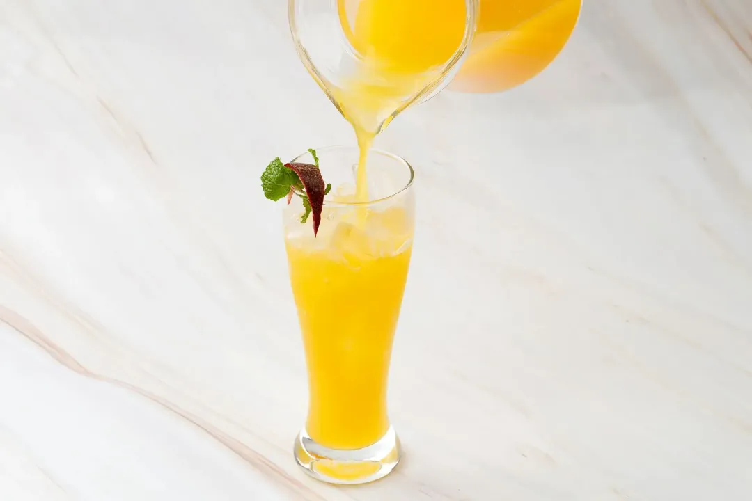 Pouring a passion and orange drink from a pitcher into a clear glass with ice