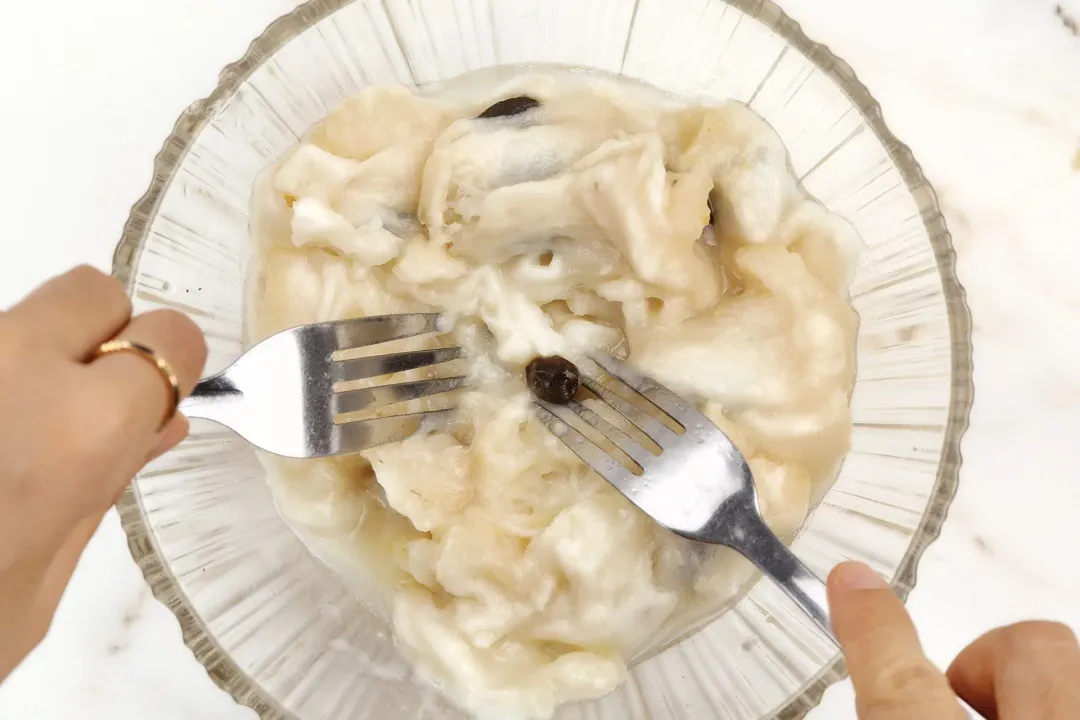 Two forks dunking into a clear bowl full of soursop flesh and seeds