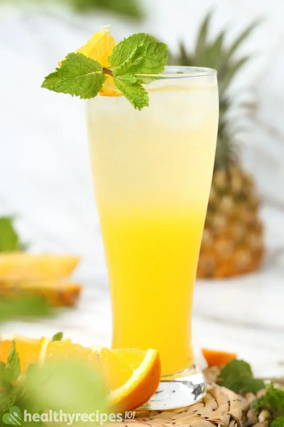 A glass of orange juice at the bottom, soda on top, garnished with orange wedges and mint sprigs