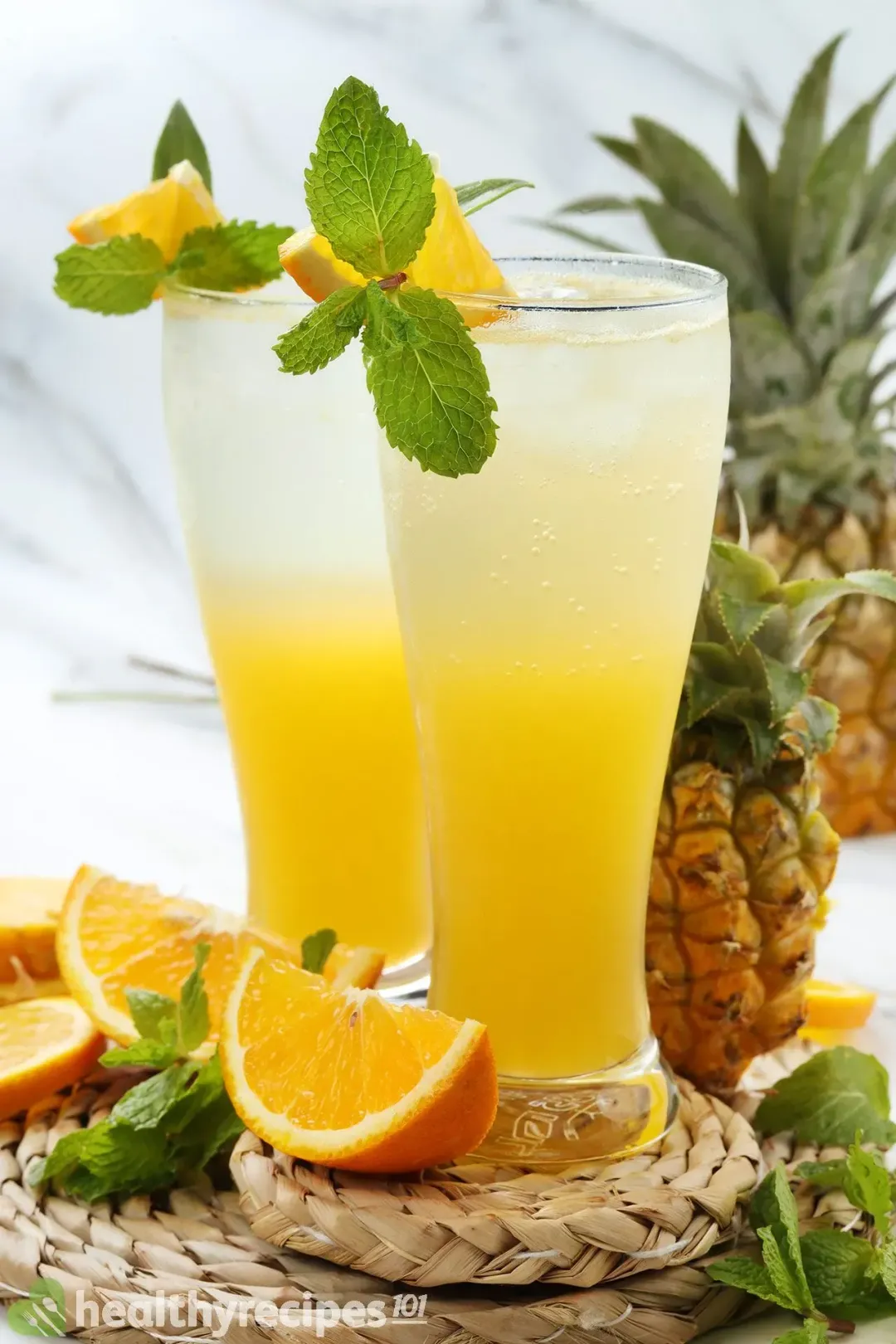 Two glasses of unstirred rum and orange juice side by side, with orange wedges and mint leaves around as garnish