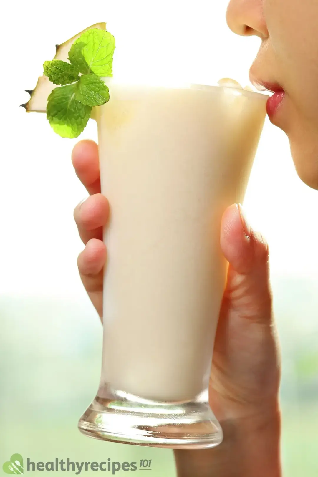 A person holding a tall glass of soursop juice close to their mouth