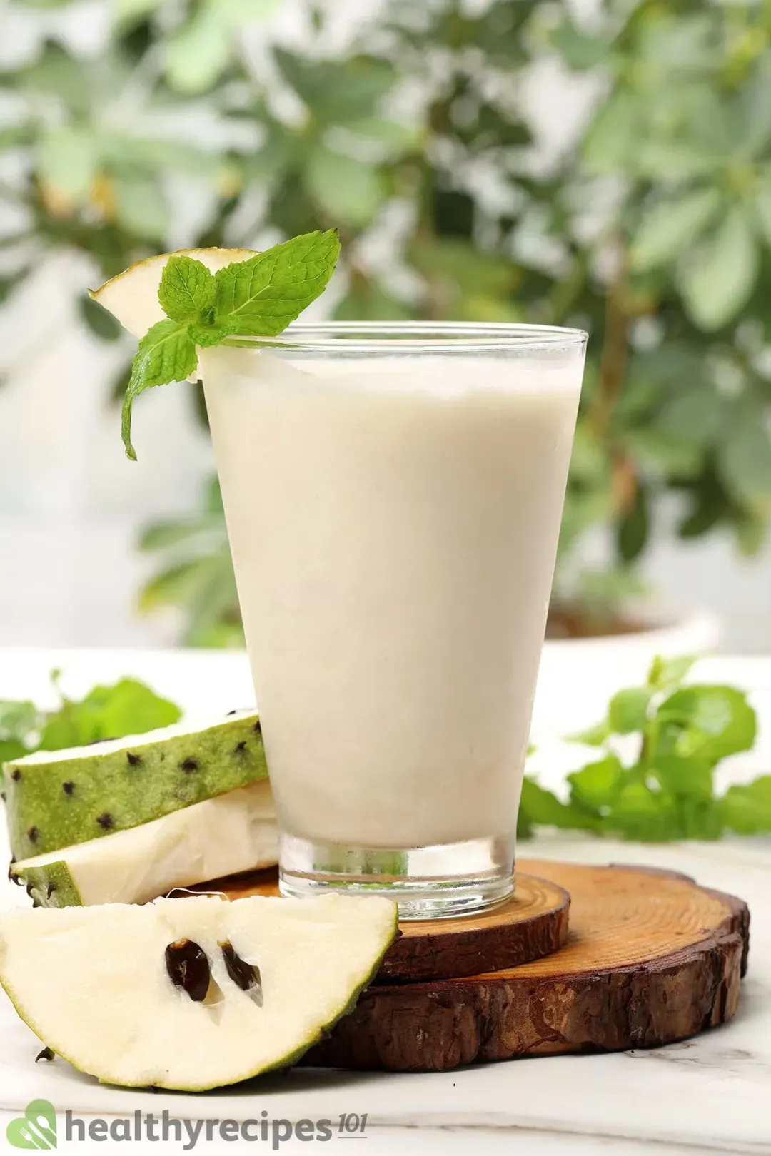 A glass of soursop juice garnished with mints and a soursop wedge, next to more soursop wedges and mints