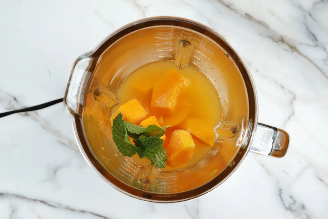 top view of papaya cubes, orange juice, mint leaves in a blender pitcher