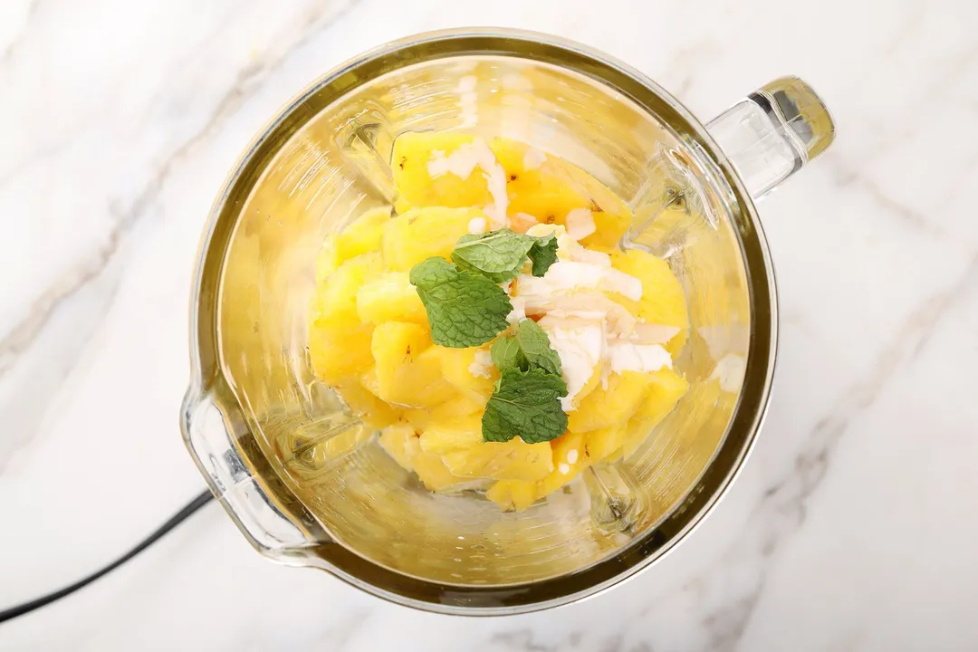 top view of pineapple cubed, mint leaves and coconut milk in a blender pitcher