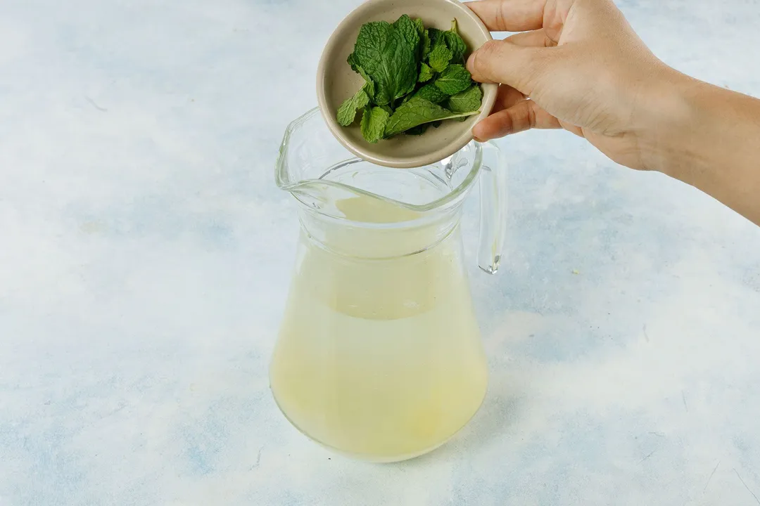 pouring mint leaves from small bowl into glass pitcher of water
