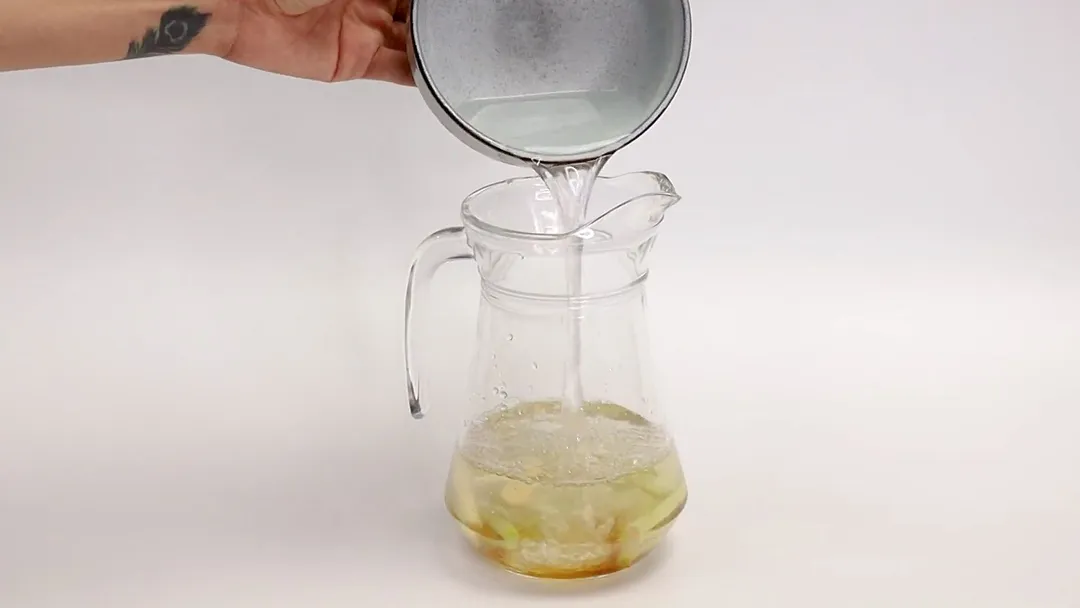 A glass jar filled with a mixture of apple cider vinegar and lemon juice, with slices of lemon and apple floating on top. The jar is placed on a wooden surface with a blurred background.