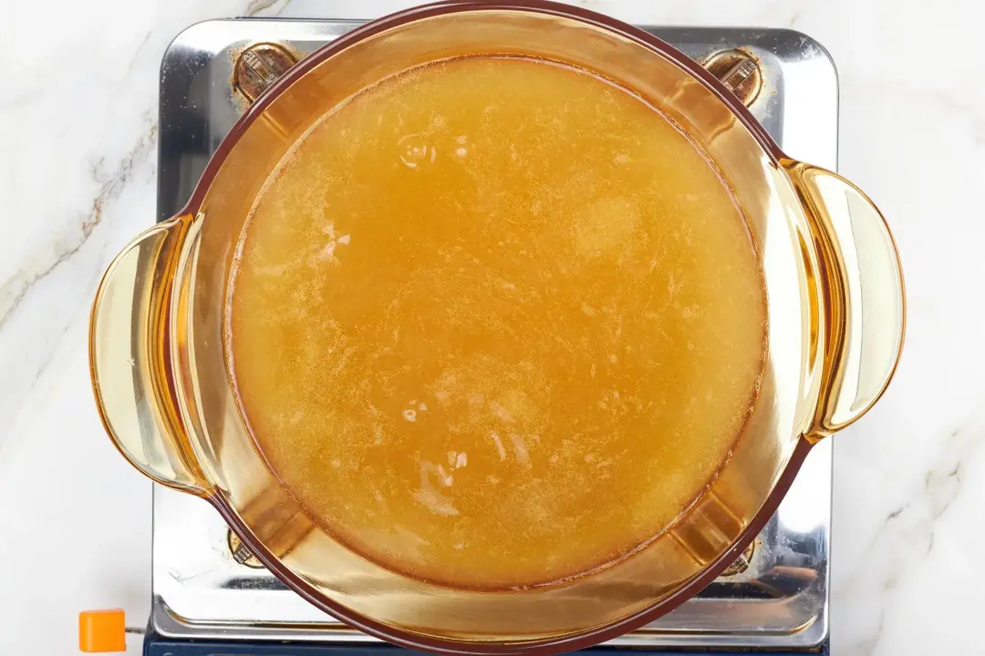 A pot of apple cider boiling in a glass pot over a gas stove