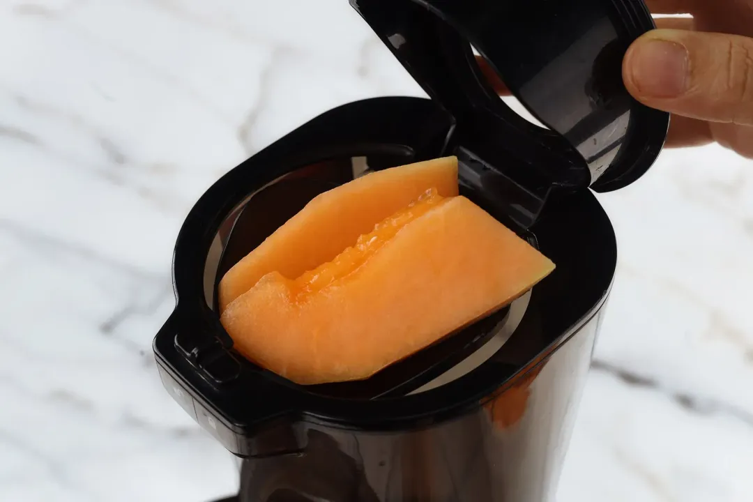 Some cantaloupe wedges in a black-colored feeder of a juicer