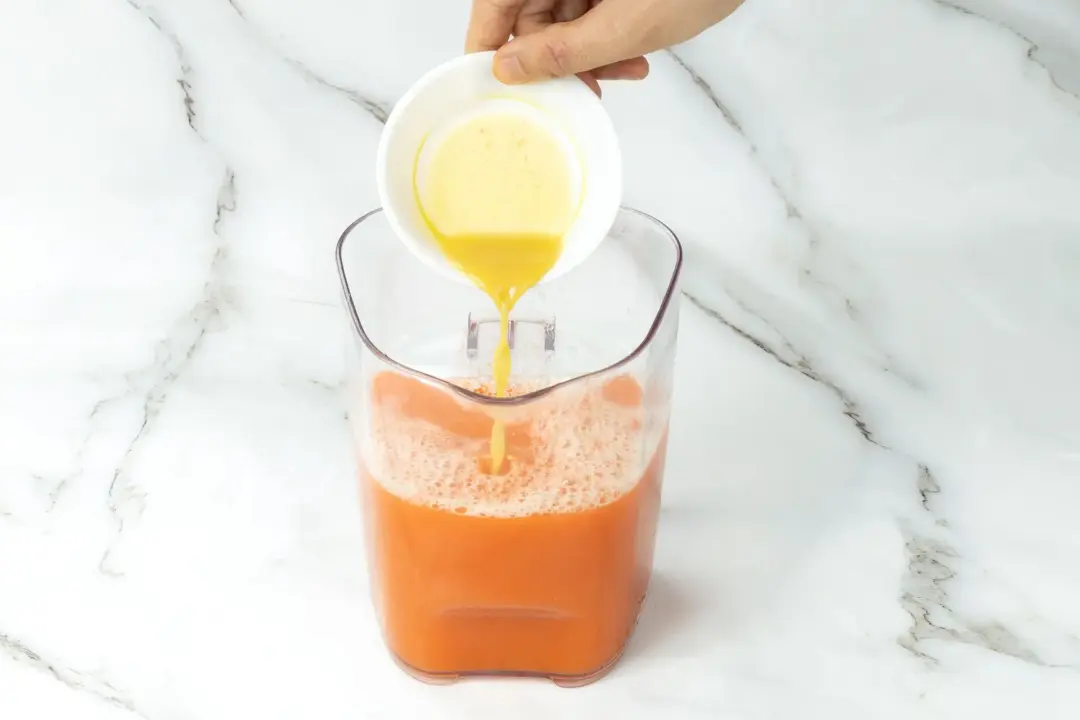 Pouring some honey into a clear pitcher of Orange carrot juice
