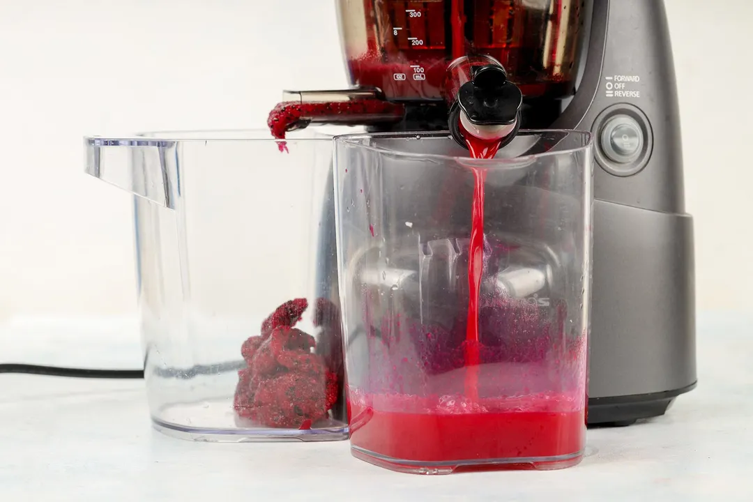 A juicer processing dragon fruit and blending the fruit into a bright pink liquid.